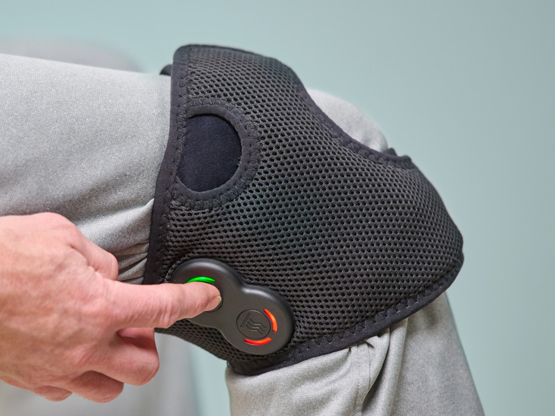 Person wearing the Activ8 Knee device on their knee, pressing a button on the controller.