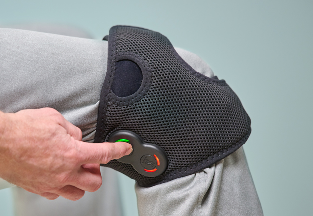 Person wearing the Activ8 Knee device on their knee, pressing a button on the controller.