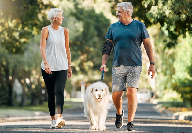 Older couple walking their dog, with the man wearing the Activ8 Elbow device.